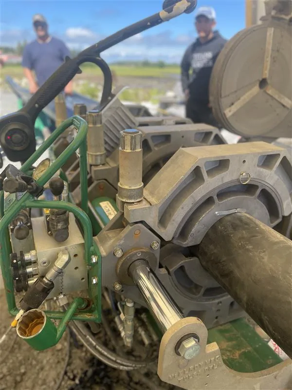 Close-up of a McElroy fusion machine clamping black HDPE pipe with two workers at an outdoor jobsite