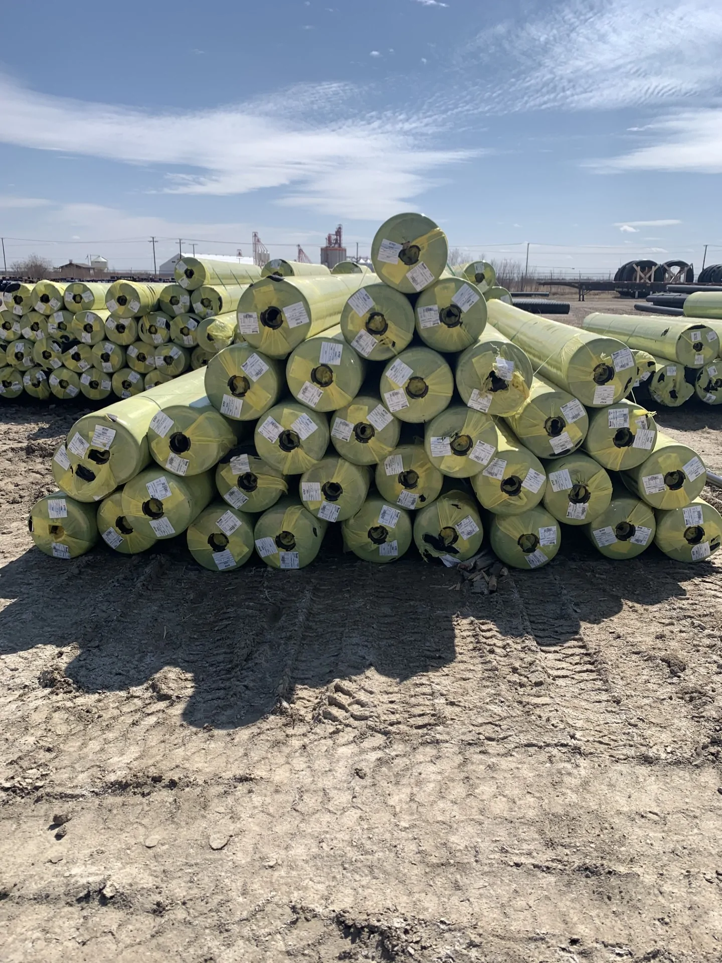 Stack of insulated pipes with yellow protective wrapping at an outdoor storage yard