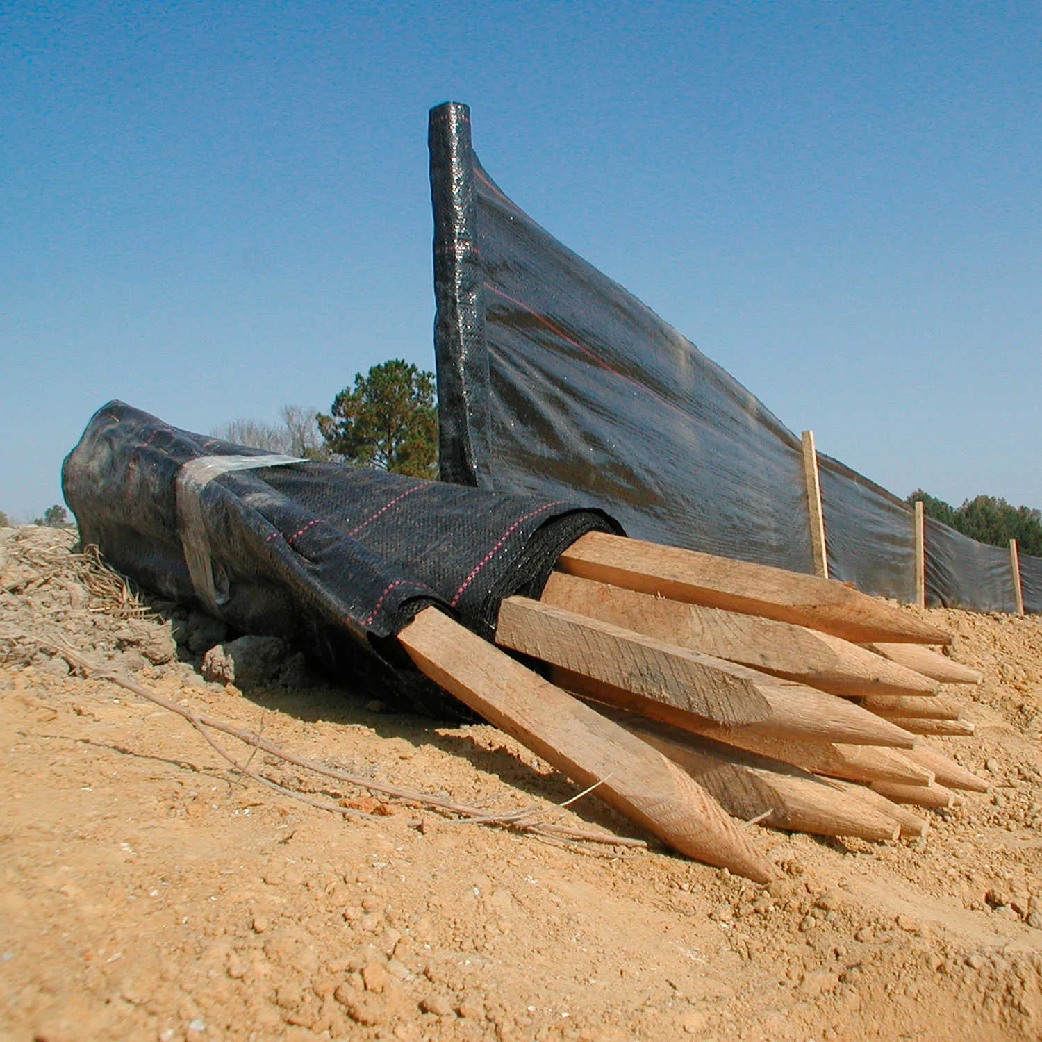 Black woven silt fence fabric with wooden stakes installed at a construction site