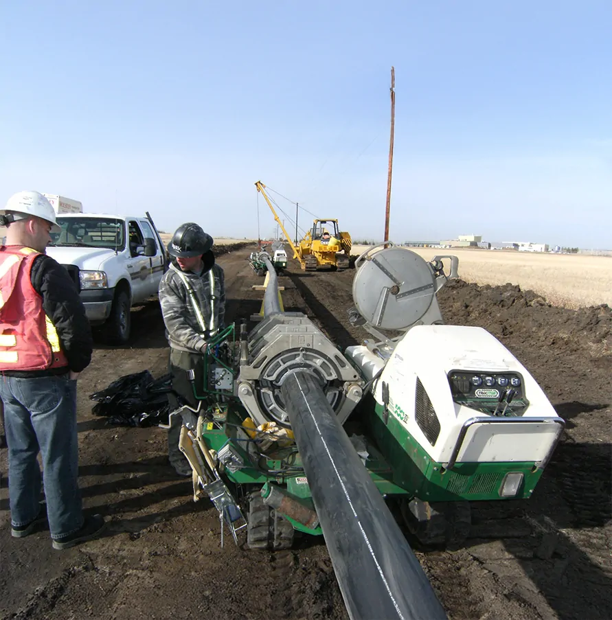 Worker fusing black HDPE pipe with a McElroy fusion machine at a roadside jobsite with a pickup truck and crew
