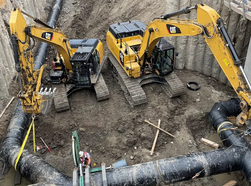 Two CAT excavators installing black HDPE pipe in an excavated trench