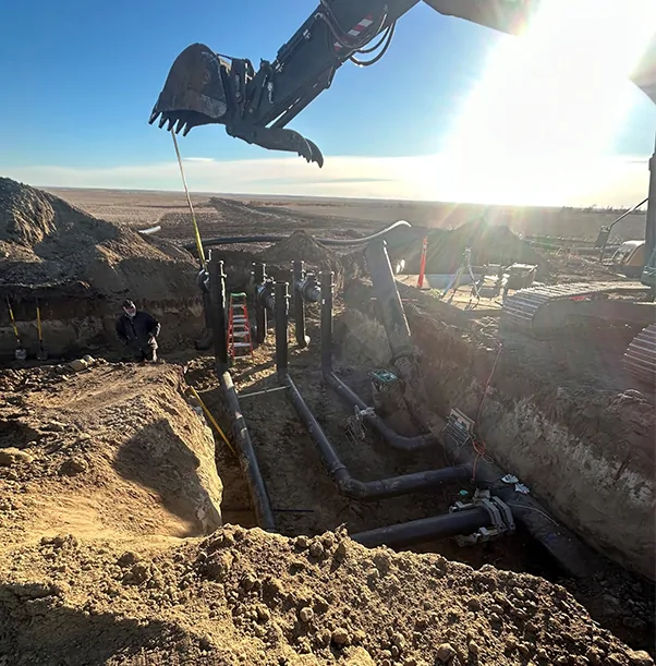 Excavator working over a trench with pipework at sunrise