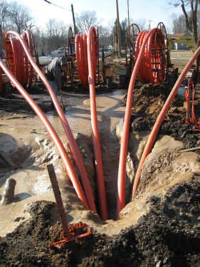 Bundle of orange HDPE conduit ducts entering an excavated trench at a construction site